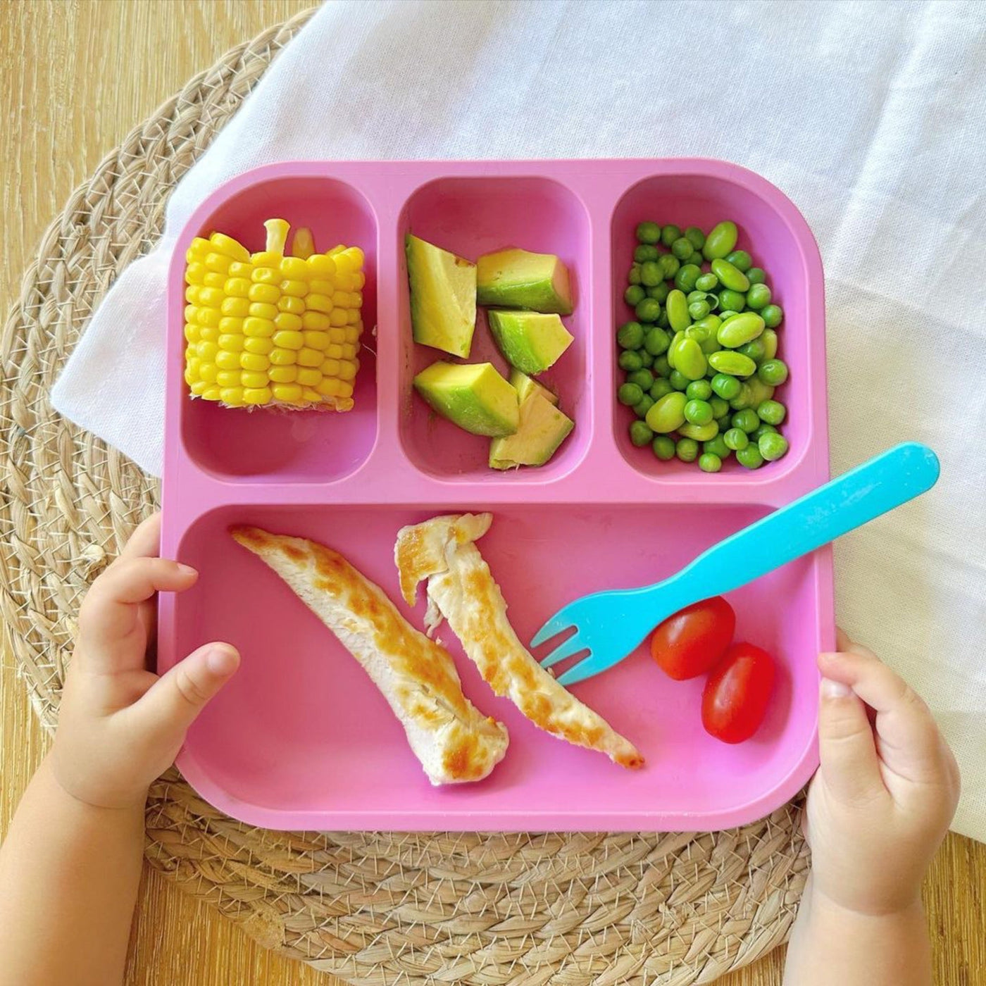a toddler holding a bobo&boo plant-based bento plate in pink that has their dinner in it 