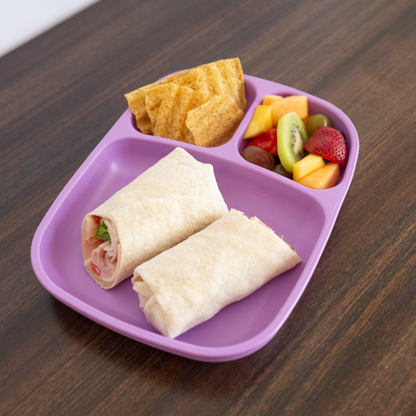 Purple divided lunch tray with wraps, chips, and fruit on a wooden surface. RePlay Recycled Divided Tray Plate - Purple
