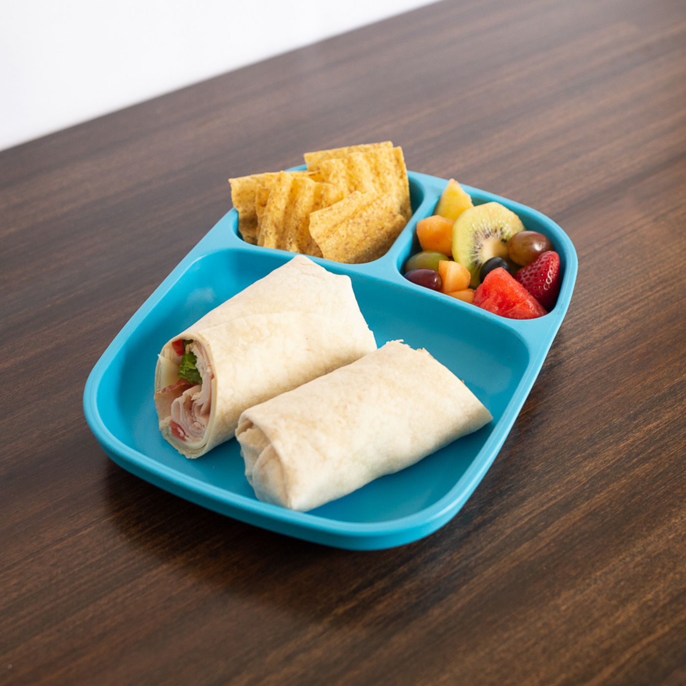 Blue divided lunch tray with wraps, chips, and fruit on a wooden surface, RePlay Recycled Divided Tray Plate - Sky Blue