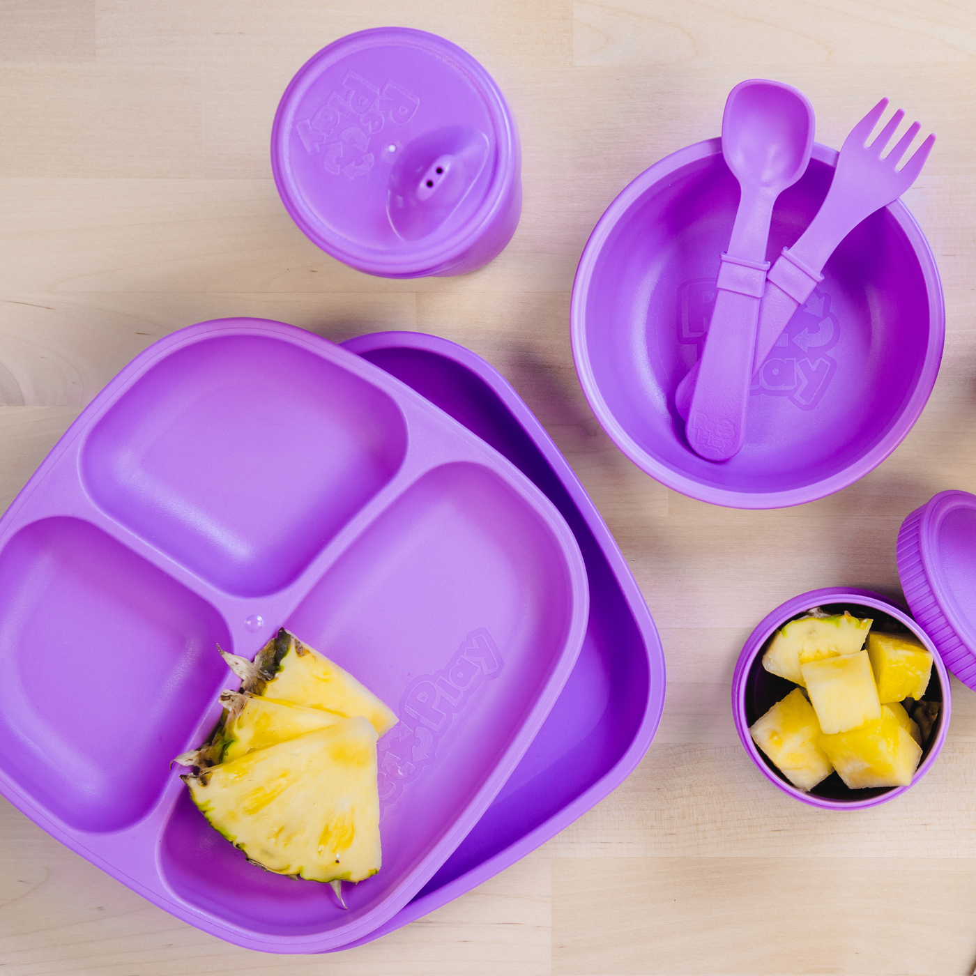 Purple children's dining set with plate, bowl, cup, and utensils on a wooden surface. RePlay Recycled Divided Plate - Purple