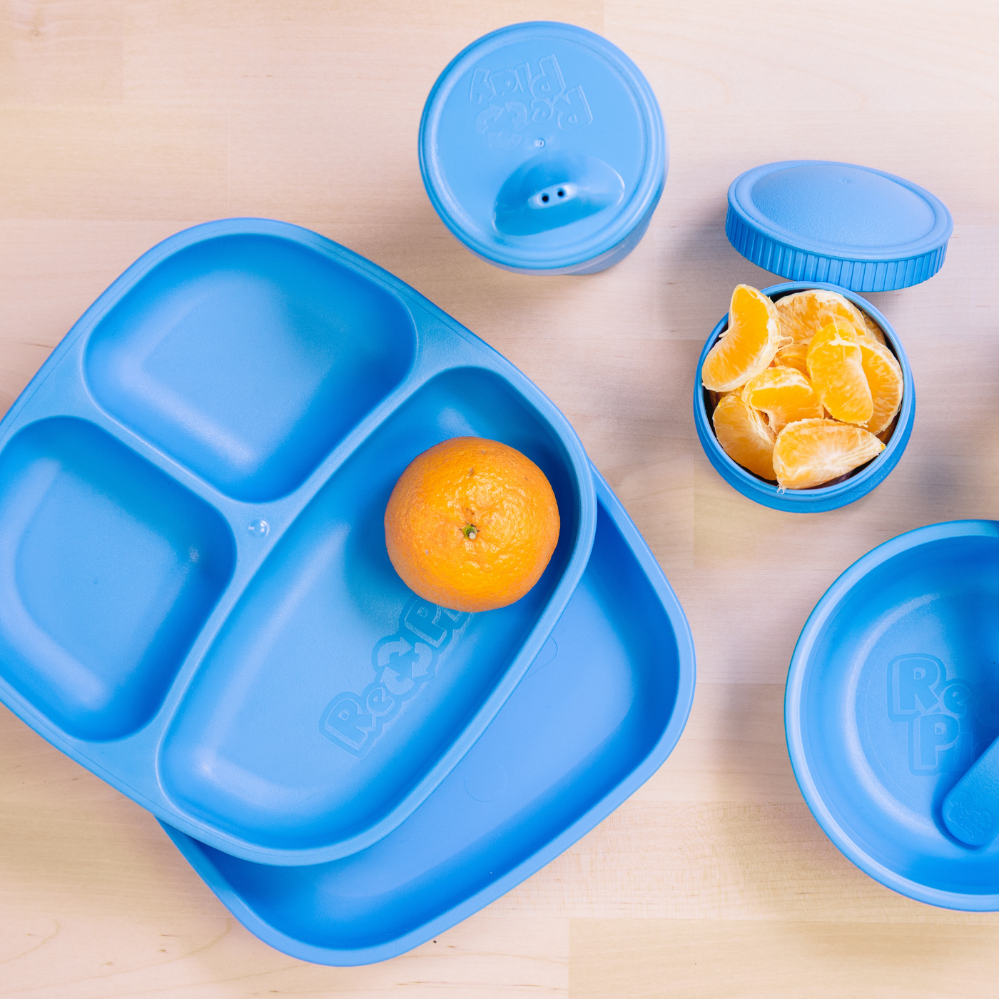 Blue children's meal set with a tray, bowls, and an orange on a wooden surface. RePlay Recycled Snack Stack (2 Pods) - Sky Blue