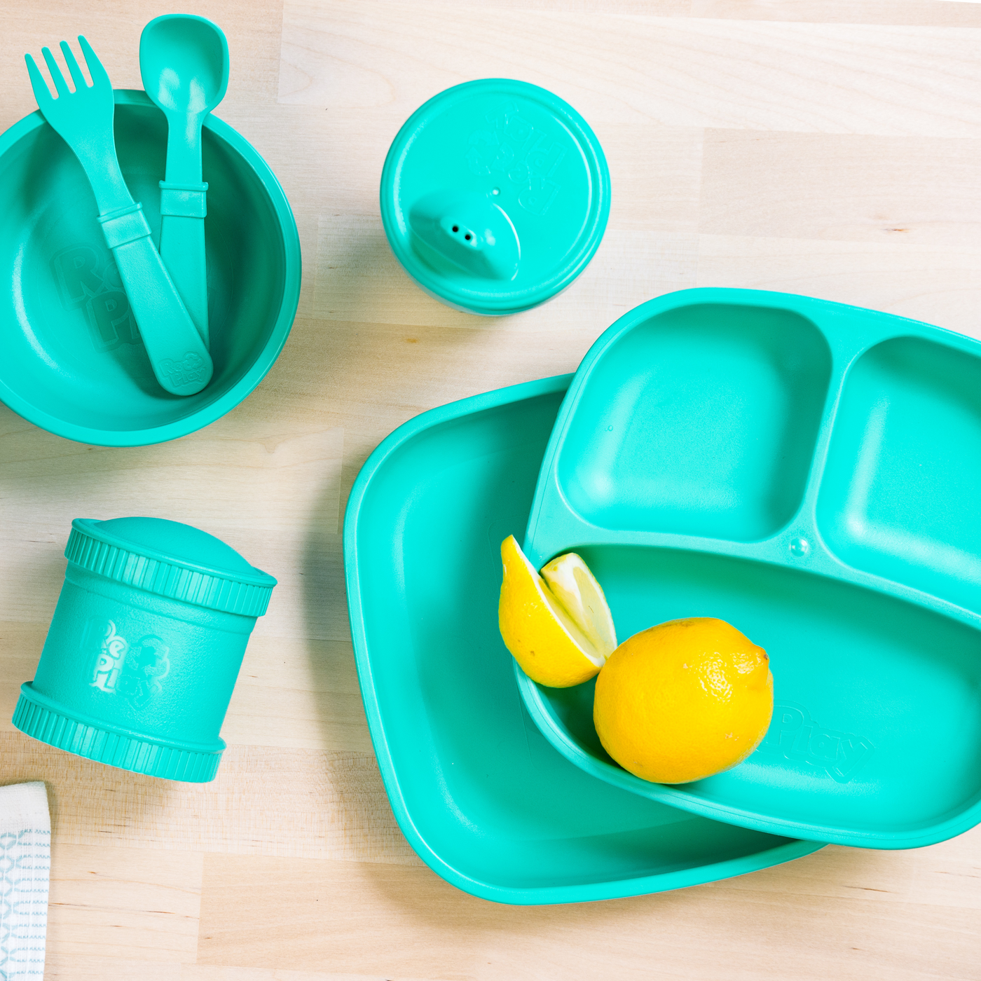 Turquoise children's dining set with plate, bowl, cups, and utensils on a wooden surface. RePlay Recycled Divided Plate - Teal